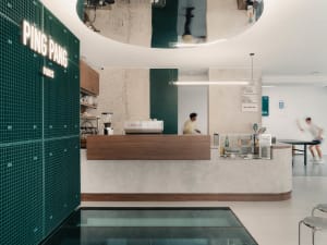 A modern cafe interior with a concrete and tile counter, featuring a coffee machine and a man working behind it.