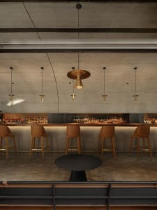 A modern bar interior featuring a concrete wall, wooden accents, and minimalist lighting.