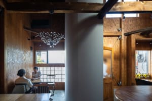 A modern restaurant interior with wooden walls and seating areas, featuring a chandelier and a glass partition.