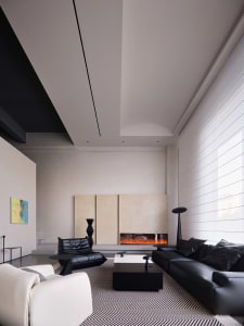 A modern living room featuring a large fireplace, a black leather sofa, a white armchair, and a black coffee table with a geo