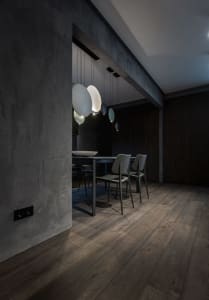 Dark concrete dining room with modern lighting fixtures and wooden floor.