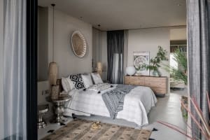 A modern bedroom featuring bohemian elements such as a patterned rug, decorative pillows, and natural wood furniture.