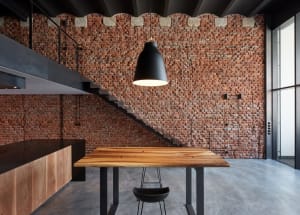 An industrial-style office space featuring a brick wall, a wooden table, concrete floor, and metal stairs.