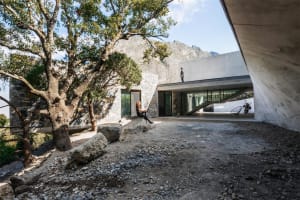 A modern house with a concrete exterior surrounded by trees and mountains.
