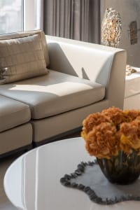 Modern living room with neutral-toned leather sofa, white coffee table, and decorative vase with orange flowers on top.