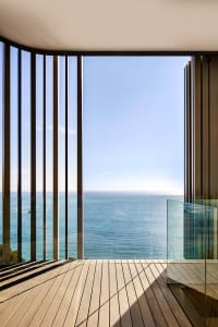 A modern terrace overlooking the ocean, featuring large glass windows and wooden flooring.