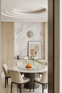 A minimalist dining room with a round glass table, marble and wood accents, and geometric wall decor.