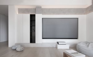 Modern living room with a large flat-screen TV, minimalist furniture, and a concrete fireplace.