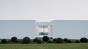 Modern residential exterior with minimalist design featuring white stucco walls and large glass window.