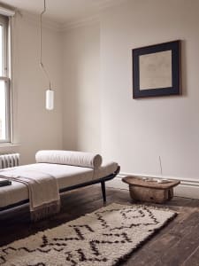 A minimalist residential room with a daybed, rug, and artwork.
