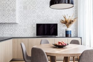 A modern minimalist kitchen with a round wooden table, chairs, and a flat-screen TV on the wall.