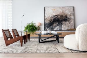 Modern living room with wooden chairs, leather sofa, metal coffee table, and abstract painting.