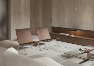 A modern living room featuring a white sofa, beige carpet, two brown leather chairs with metal frames, a wooden bench with a 