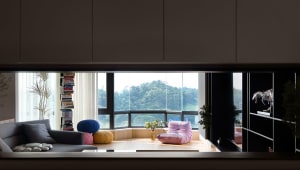 A modern living room with wooden flooring, glass walls, and colorful fabric seating and decorations.