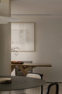A modern dining room featuring a live-edge wooden table with a black circular dining table and woven chairs.
