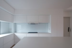 Modern kitchen with sleek, white countertops and transparent backsplash.