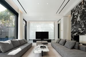 A modern living room with a marble coffee table, gray sofas, and a large screen television.
