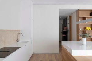 Modern residential kitchen with minimalist design, featuring white countertops and cabinetry, illuminated by natural light.