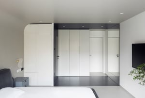 A modern minimalist bedroom with white walls, a black headboard bed, and a minimalistic design.