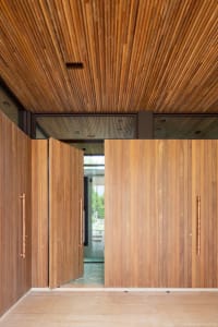 Modern entryway featuring large wooden doors with metallic handles and a ceiling made of vertical wooden slats.