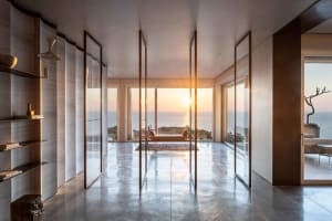 Sunlit room with concrete floor, glass walls, and ocean view.