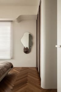 A minimalist bedroom featuring a bed with a wooden frame and a unique shaped mirror hanging on the wall.