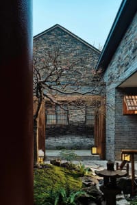 A stone building with a brick facade and a large tree in front, creating a sense of depth and connection between nature and architecture