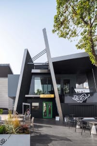 A modern building with a green door and glass facade, featuring a bright and airy interior with natural light and several chairs