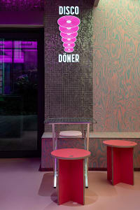 A cozy dining area with a pink table surrounded by metal chairs, natural light from a window, and a warm atmosphere