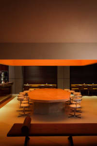 A modern restaurant interior with a large wooden dining table surrounded by chairs in a stylish setting