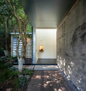 A calm and inviting interior space with a white wall, wooden doorway, stone walkway, potted plants, and a bench, creating a serene atmosphere