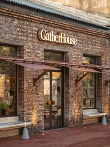 A traditional storefront with a brick exterior and a cozy interior featuring chairs and natural/artificial lighting