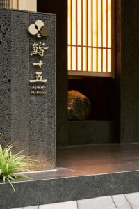 A stone entrance wall with Chinese characters, two large rocks, and a doorway create a traditional and cultural atmosphere