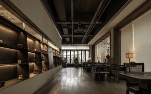 A well-lit lobby with a wooden floor, several chairs, and potted plants, designed for socializing or gatherings