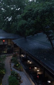 Cozy Asian restaurant with a black roof, red trim, and potted plants, featuring a dining area with tables and chairs and wine glasses
