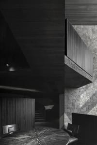 Black and white photo of a building with a concrete staircase leading to a lower level, creating a sense of depth and intrigue