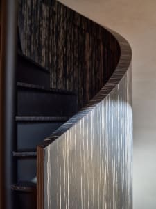 A warm and inviting interior staircase with wooden stairs and a black railing, set against a unique wall design
