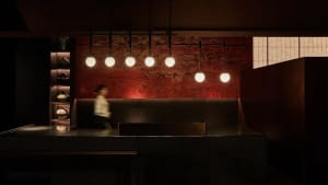 A restaurant interior with a counter and pendant lights, two people interacting with the space