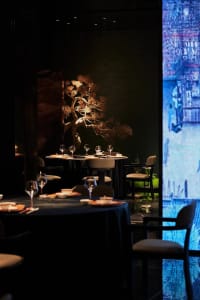 A sophisticated dining area with a large wooden table surrounded by chairs and wine glasses, set in a restaurant environment