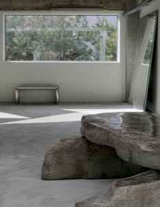 A calm and inviting space with a large rock in the center, surrounded by a bench and a dining table, with a mix of living and dining areas