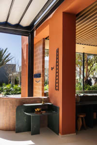 A public bathroom with a brick-patterned wall, a metal sink, and a towel rack, with two people present