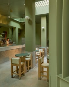 Inviting restaurant interior with green walls, wooden tables, and a bar area, featuring bottles and comfortable seating