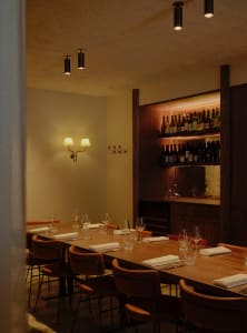 Dimly lit dining space with tables, chairs, and wine glasses, featuring a modern and sophisticated design