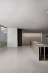 A clean and minimalist lobby with white walls, a large window, and an empty space