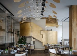 Dining area with multiple tables, chairs, and potted plants, surrounded by gold-colored walls