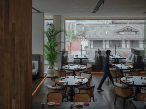 A bustling Asian restaurant interior with wooden tables, chairs, and dining areas, set up for guests with bowls and a welcoming atmosphere