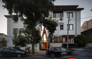 A house with two cars parked outside and two people present, featuring a large window that lets in natural light