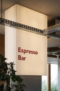 Cozy bar interior with a red sign reading Espresso Bar, white walls, and two potted plants adding greenery
