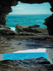 A serene coastal landscape with a grey rocky archway and blue ocean in the background