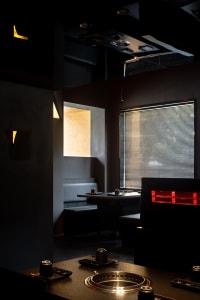 Dark and intimate restaurant interior with concrete walls, multiple chairs and tables, a bar, and two couches